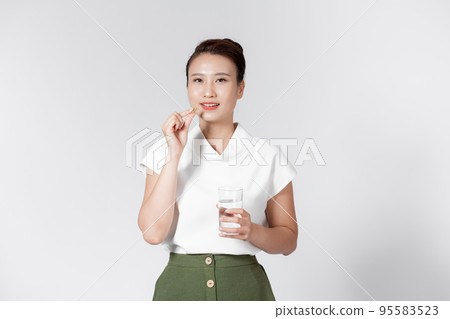 Beautiful smiling woman taking vitamin pill and holding glass of fresh water in morning. 95583523