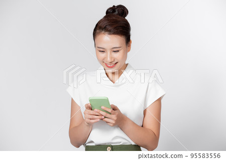 Happy young woman writing message on smartphone isolated against white wall Happy young woman writing message on smartphone isolated against white wall 95583556