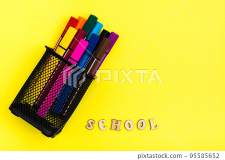 Back to school. Container with markers and the word school from wooden letters on a yellow background. Top view 95585652