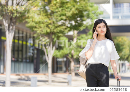 一位女商人，一邊背著背包，一邊拉著手提箱，一邊打電話給智能手機 95585658