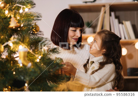 Happy mother and little daughter decorating christmas tree at home. Happy mother and little daughter decorating christmas tree at home. 95586316