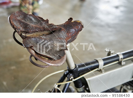 Completely worn old broken leather saddle on antique bike 95586430