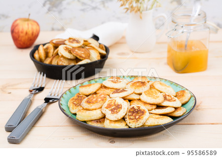 Trend breakfast. Dutch mini pancakes on a plate and a frying pan with them on a wooden table. Trend breakfast. Dutch mini pancakes on a plate and a frying pan with them on a wooden table. 95586589