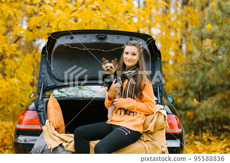 Happy girl and dog sitting in the trunk of a car in nature. Friendship of a man and a dog, travel, camping on an autumn background. Moment of happiness 95588836