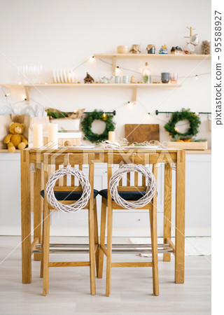 Wooden dining table with chairs decorated for Christmas and New Year in a bright Scandinavian style dining room Wooden dining table with chairs decorated for Christmas and New Year in a bright Scandinavian style dining room 95588927