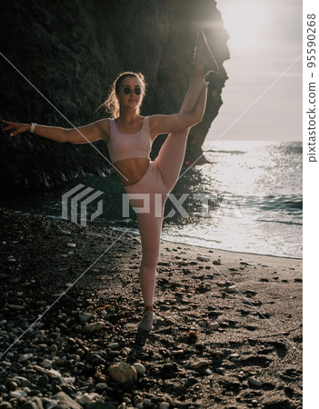 Young woman with black hair, fitness instructor in pink leggings and tops doing stretching and pilates on volcanic rocks near the sea on sunset. Female fitness yoga routine concept. Healthy lifestyle. 95590268