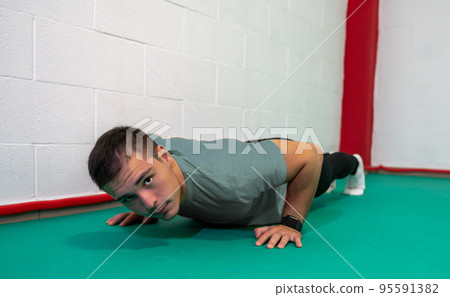 Determined strong young man doing push-ups and looking at camera. He is dressed in an grey shirt and black jumpsuit. Copy space Determined strong young man doing push-ups and looking at camera. He is dressed in an grey shirt and black jumpsuit. Copy space 95591382