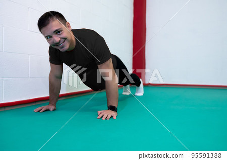 Portrait of a strong determined young man doing push-ups and looking at camera smiling. He is dressed in an black shirt and a black suit. Copy space Portrait of a strong determined young man doing push-ups and looking at camera smiling. He is dressed in an black shirt and a black suit. Copy space 95591388