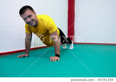 Portrait of a strong determined young man doing push-ups and looking at camera smiling. He is dressed in an yellow shirt and a black suit. Copy space Portrait of a strong determined young man doing push-ups and looking at camera smiling. He is dressed in an yellow shirt and a black suit. Copy space 95591394