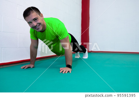Portrait of a strong determined young man doing push-ups and looking at camera smiling. He is dressed in an green shirt and a black suit. Copy space Portrait of a strong determined young man doing push-ups and looking at camera smiling. He is dressed in an green shirt and a black suit. Copy space 95591395