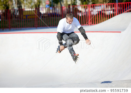 Mature male inline roller training in public skate park. Practicing jumps, tricks. Concept of active lifestyle, sport, hobbies. Mature male inline roller training in public skate park. Practicing jumps, tricks. Concept of active lifestyle, sport, hobbies. 95591739