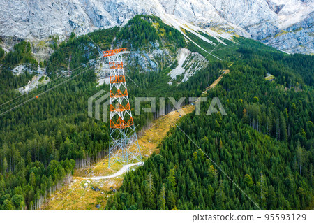 Power line pylon high in the mountains surrounded by trees, aerial view. delivery of electricity to hard to reach areas Power line pylon high in the mountains surrounded by trees, aerial view. delivery of electricity to hard to reach areas 95593129