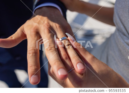 mans hand putting a wedding ring on the brides finger. 95593535