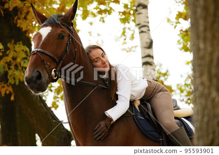 Autumn landscape, beautiful brunette girl with long hair posing with a red horse in the forest. 95593901