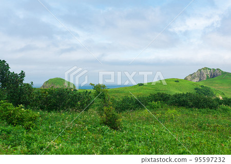 natural landscape of Kunashir island with grassy hills, volcanic rocks, volcano in the clouds and ocean in the distance natural landscape of Kunashir island with grassy hills, volcanic rocks, volcano in the clouds and ocean in the distance 95597232