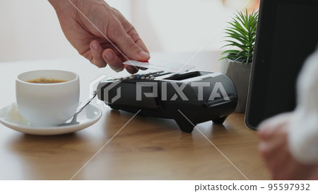 Close up woman makes coffee for a customer who pay using credit card contactless payment spending money in cafe with digital transaction service. Close up woman makes coffee for a customer who pay using credit card contactless payment spending money in cafe with digital transaction service. 95597932