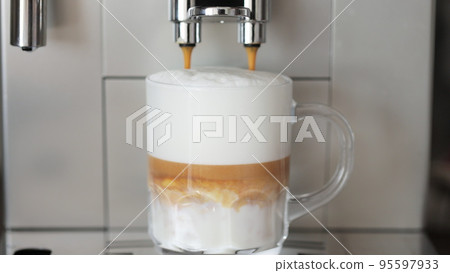 Close up shot of coffee pouring into glass cup with milk, making cappuccino using the automatic coffee machine. Beverage drink for breakfast. Close up shot of coffee pouring into glass cup with milk, making cappuccino using the automatic coffee machine. Beverage drink for breakfast. 95597933