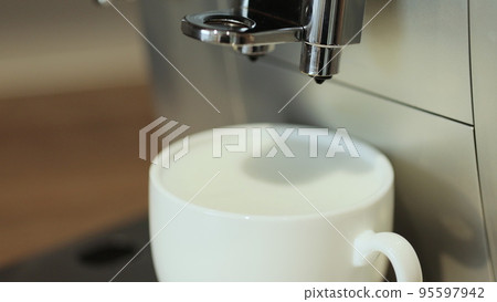 Making cappuccino using automatic coffee machine. Coffee is pouring into cup with frothed milk or cream close-up. Beverage drink for breakfast. 95597942