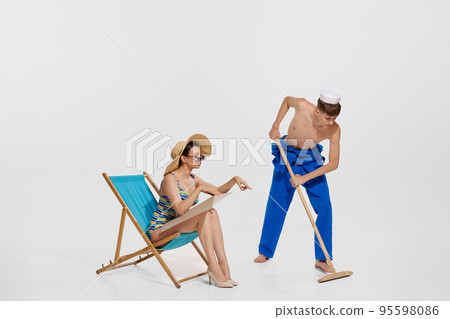 Portrait of beautiful young woman in swimming suit pointing at floor for young shirtless sailor washing deck isolated on white background 95598086