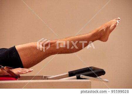 Fit man doing a lunge stretch yoga pilates exercise to strengthen and tone his muscles using a reformer in a gym 95599028