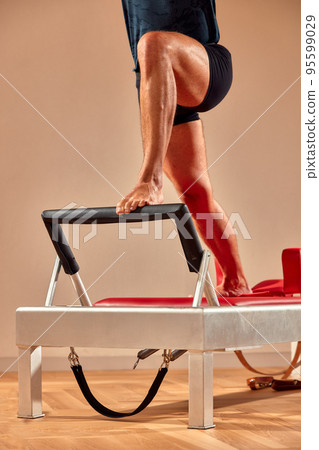 Fit man doing a lunge stretch yoga pilates exercise to strengthen and tone his muscles using a reformer in a gym Fit man doing a lunge stretch yoga pilates exercise to strengthen and tone his muscles using a reformer in a gym 95599029