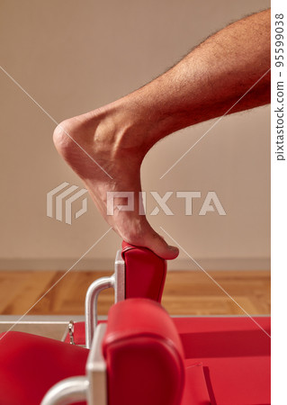 Fit man doing a lunge stretch yoga pilates exercise to strengthen and tone his muscles using a reformer in a gym 95599038