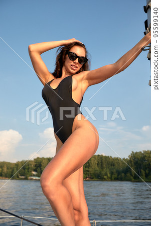 Fashion lifestyle portrait of young brunette woman in the sexy swimsuit posing at white luxury yacht 95599140