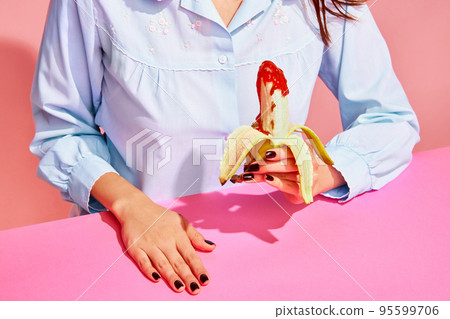 Food pop art photography. Young woman tasting banana with tomato ketchup isolated on pink background. Vintage, retro style interior. Surrealism Food pop art photography. Young woman tasting banana with tomato ketchup isolated on pink background. Vintage, retro style interior. Surrealism 95599706