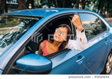 A young angry woman peeks out of the car window A young angry woman peeks out of the car window 95600648