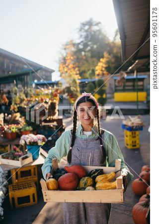 Farmer woman holds a wooden box with pumpkins in hands Farmer woman holds a wooden box with pumpkins in hands 95601178