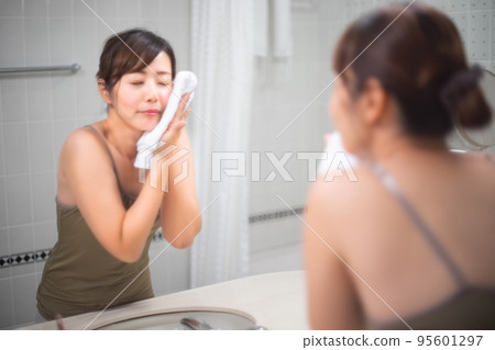 Portrait of a woman wiping her face with a towel after washing her face in front of a mirror 95601297