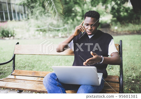 Young African man talking on phone disputing over computer, stressed, unsatisfied. Disappointed, confused, angry male arguing with technical online support or customer service. Bad connection concept 95601381