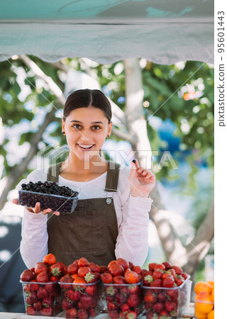 Young positive saleswoman at work, holding currants in her hands Young positive saleswoman at work, holding currants in her hands 95601443