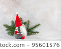 Christmas gnome in red hat side view with fir branch holiday card on light winter background 95601576