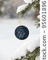 Hanging blue glitter Christmas ball on spruce and over blurred background 95601896