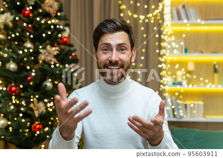 Closeup happy man talking on a video call looking web camera and talking with friends, at home for Christmas sitting on a sofa in the living room near the Christmas tree, on New Year's holidays. 95603911