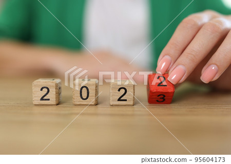 Female hand flipping of wooden cube block change from 2022 to 2023 95604173