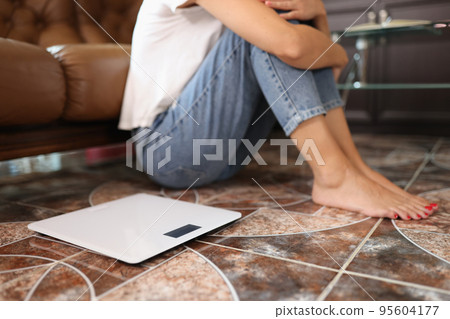 Woman sitting on floor near electronic scales Woman sitting on floor near electronic scales 95604177