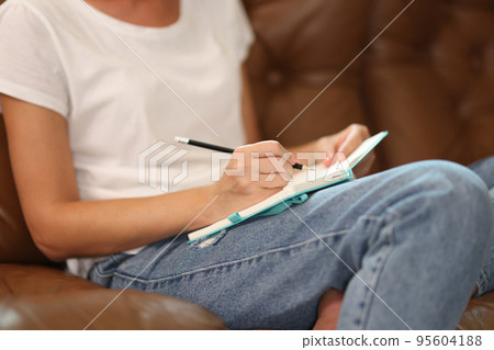 Woman sitting on sofa and writing something on notepad 95604188