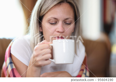 Woman sitting on sofa wrapped in blanket and drinking tea Woman sitting on sofa wrapped in blanket and drinking tea 95604190