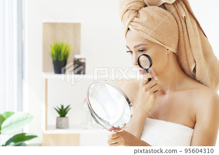 Beautiful face of a young woman with clean fresh skin holding a magnifying glass 95604310