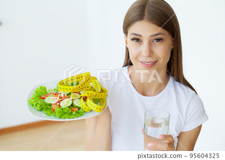 Portrait young woman with vegetarian vegetable salad and measure tape Portrait young woman with vegetarian vegetable salad and measure tape 95604325