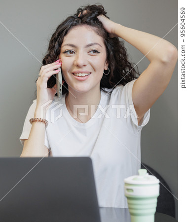 woman is working on a laptop, talking on the phone and smiling. a happy successful Spanish woman entrepreneur woman is working on a laptop, talking on the phone and smiling. a happy successful Spanish woman entrepreneur 95604569