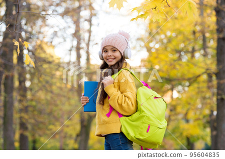 kid listen music in autumn park. fall is a time for study. back to school. concept of online education. child carry books for study. girl in earphones with school bag 95604835