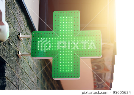 Drugstore signboard on building. Pharmacy green light cross board. Store decoration of downtown. Logo of city dispensary. Sunlight on background. 95605624