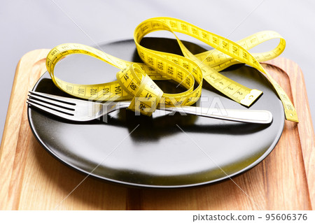 Yellow measure tape belted around metal fork on black plate 95606376