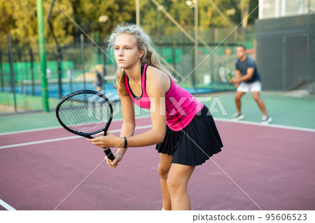 Focused young woman playing tennis on court, preparing to hit to return ball. Concept of sport training Focused young woman playing tennis on court, preparing to hit to return ball. Concept of sport training 95606523