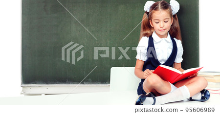 Young cute girl sitting at the table and reading a book 95606989