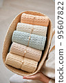 Woman puts in a wicker basket a composition of neatly rolled bathroom towels made of natural muslin. Natural, soft, air and stylish home textiles. 95607822
