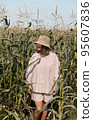 Young girl in a linen suit and a hat on a summer sunny day stands in a corn field. Love of travel and adventure. 95607836